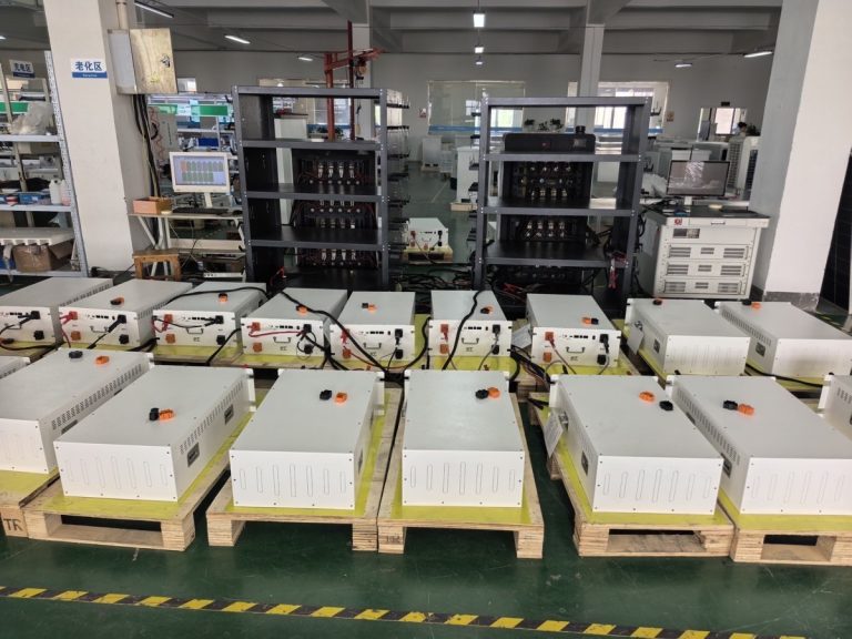** Weltrus C&I ESS factory floor showing battery modules on pallets, aging racks, and test monitors