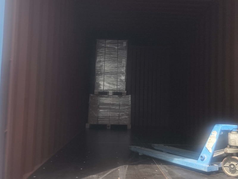 Stretch-wrapped pallets inside a shipping container with a pallet jack during factory loading