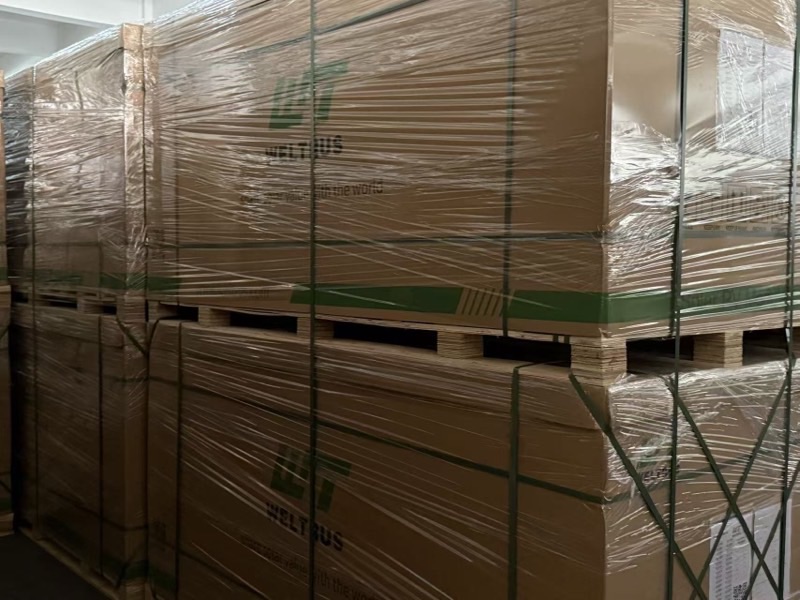 Stretch-wrapped Weltrus solar module pallets with green straps in the factory warehouse